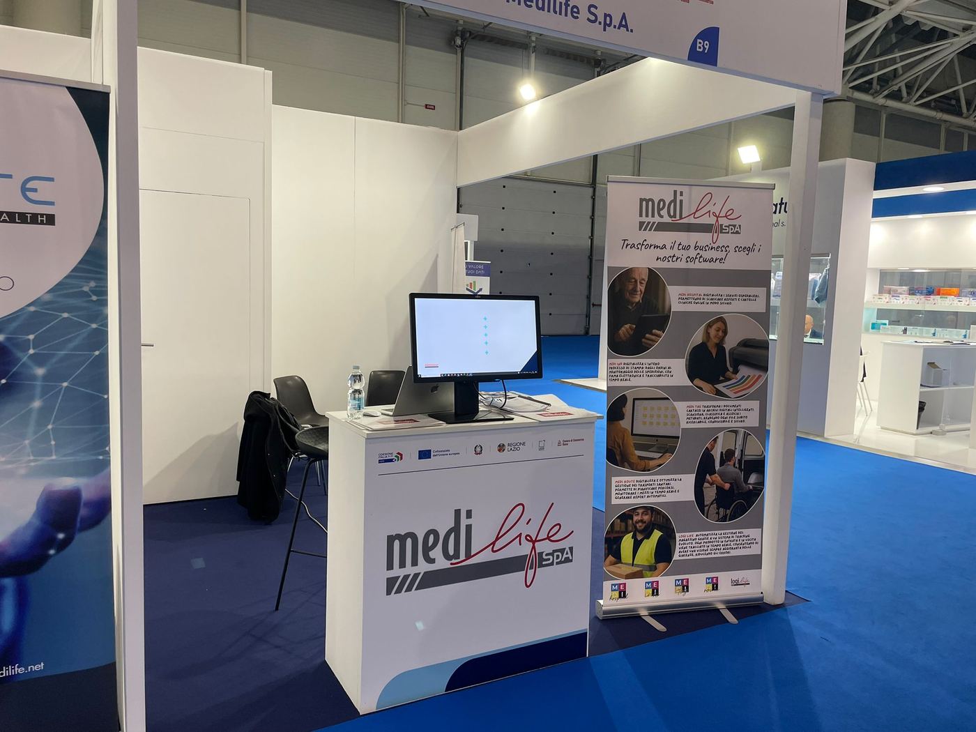 Lo stand Medilife in una fiera, con il banco informativo e il roll-up dei software